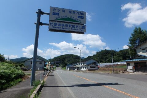 木次線「三井野原駅」近くの国道314号を撮影しました。奥に見える分岐を左折すると「三井野原駅」です。分水嶺（奥側が江の川水系、手前側が斐伊川水系で、どちらも日本海へ流れます）であることを示す看板が向かって右に立っています。