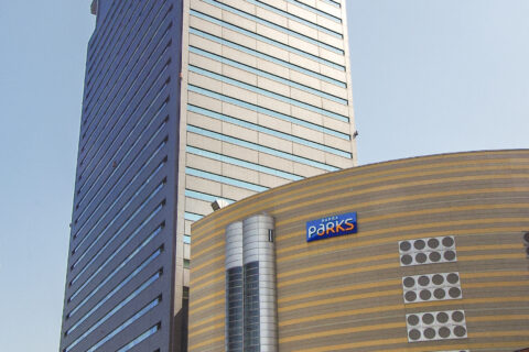 大阪市浪速区難波中2丁目のパークスタワー。なんばパークス1期事業で建設されたオフィスビル。2003年8月竣工。地上30階・地下3階、高さ約149m。建築主は南海都市創造、高島屋。設計は日建設計。施工は竹中工務店、南海辰村建設。ビル南西側をパークス通（区画道路第1号線・南北線）を挟んで北東方向へ撮影、PTLens 1.5.2と Adobe Photoshop Lightroom 4でレンズ収差・遠近法と色調を調整した。